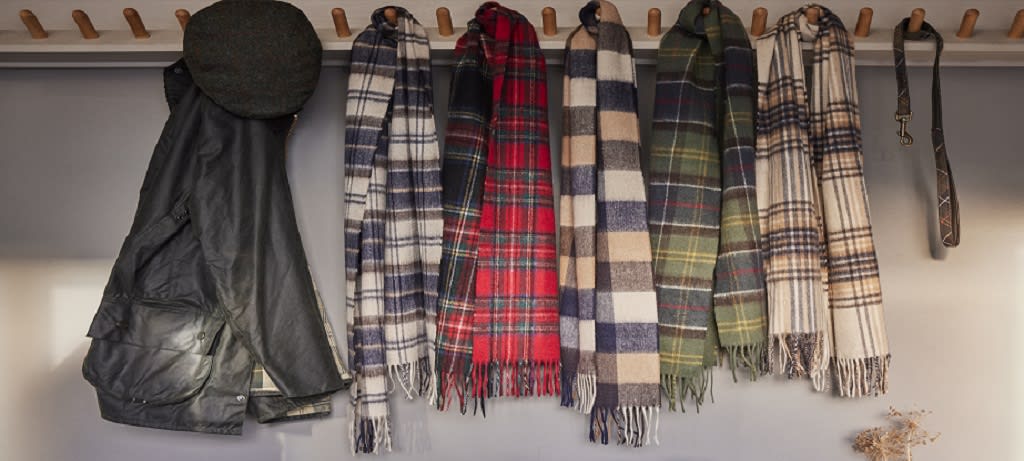 Winter Essentials - collection of Barbour scarves hanging up with wax jacket, flat cap and dog lead.